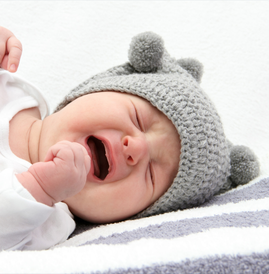 Baby crying and wearing a knit hat
